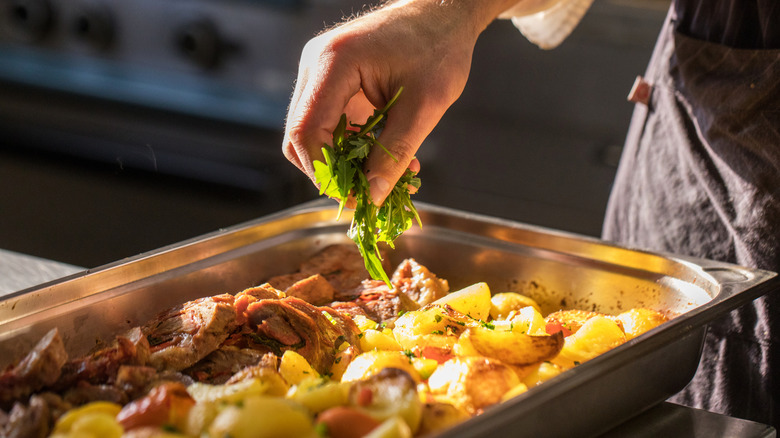 Adding fresh herbs to roasted meat and potatoes in pan