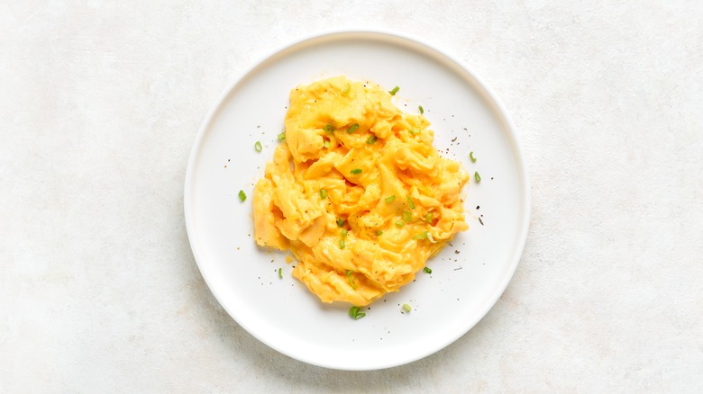Scrambled eggs on white plate on light background.