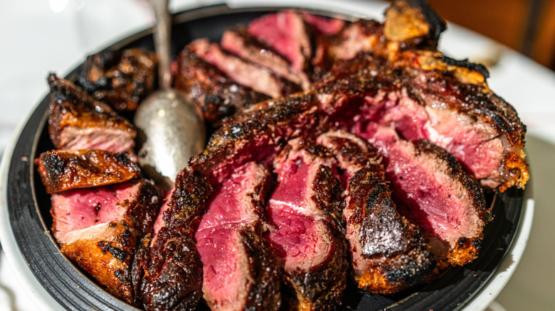 Charred T-bone steak cooked medium rare sliced on plate.