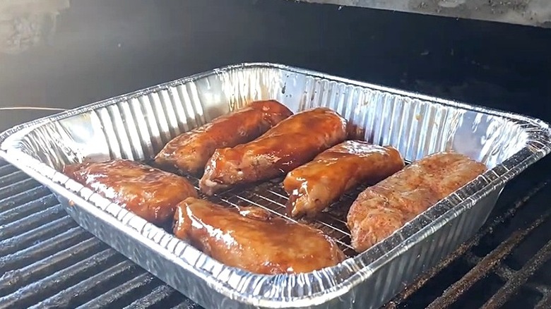 Turkey ribs in foil cooking container on grill.