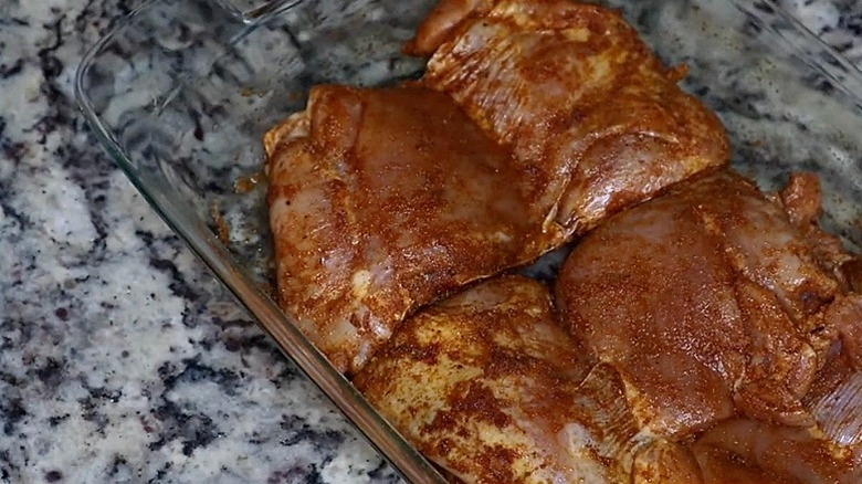Raw turkey rib meat marinating with a dry rub in a glass baking dish set on counter.