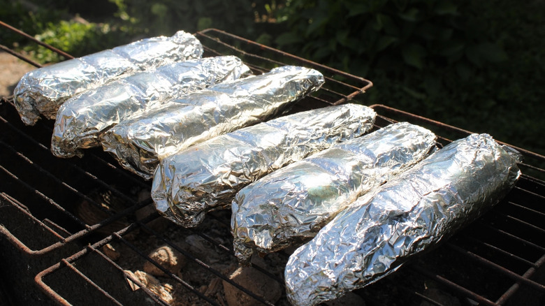 Six individual foil-wrapped pieces of meat on grill racks.