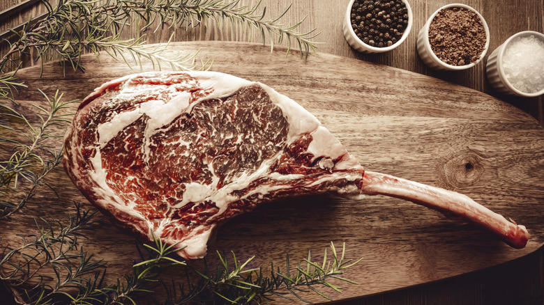 A large, well marbled, dry-aged steak sits atop a wooden cutting board.