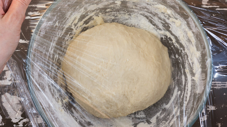 Dough in glass bowl covered with cling wrap