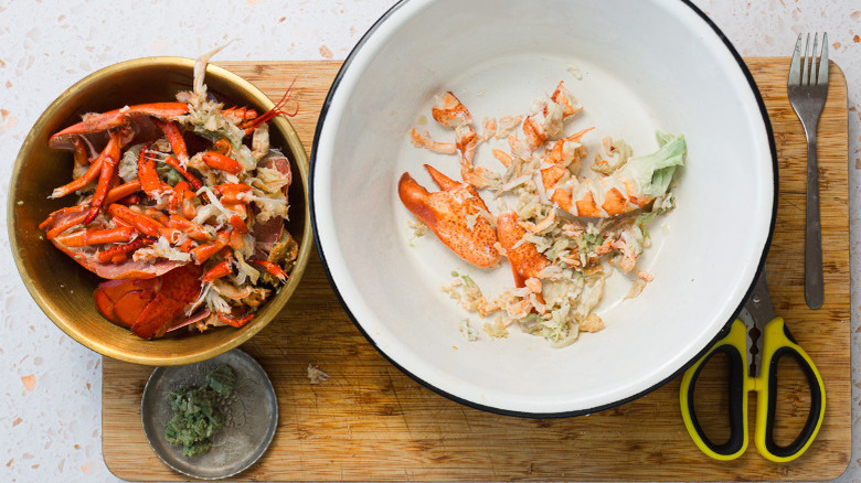 Lobster meat in bowl besides lobster shells in bowl and scissors