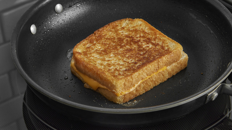 Classic grilled cheese sandwich made with American, processed cheese and white bread, cooking in a nonstick frying pan on a stovetop.