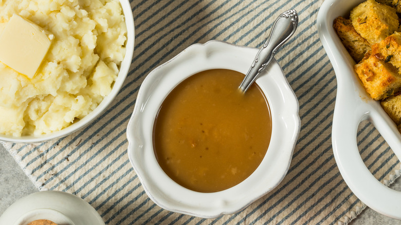 A bowl of gravy on a table next to sides including mashed potatoes