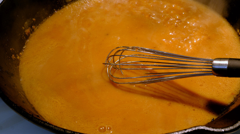 A wire whisk sitting in a pot of gravy on a stove