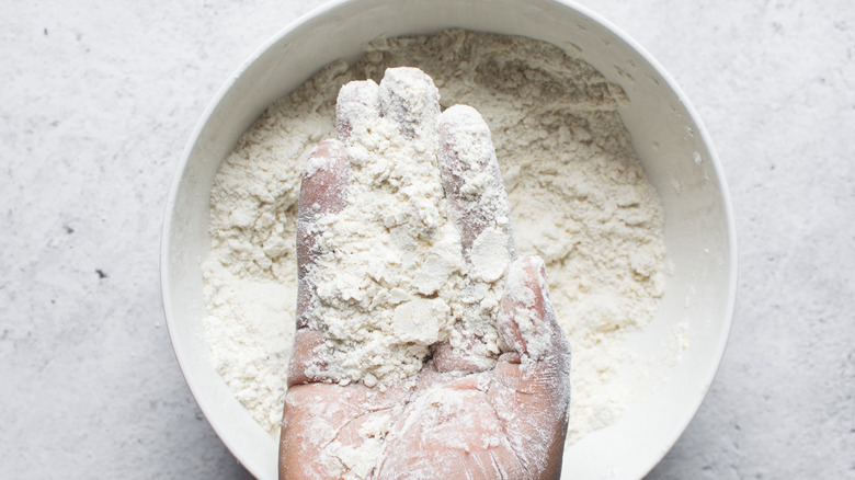 Butter and flour being mixed together in a bowl with a hand holding crumbs.