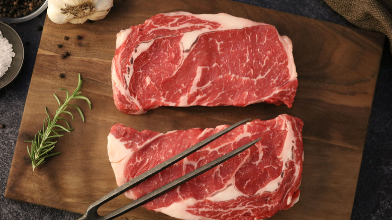 two ribeye steaks on a wooden cutting board