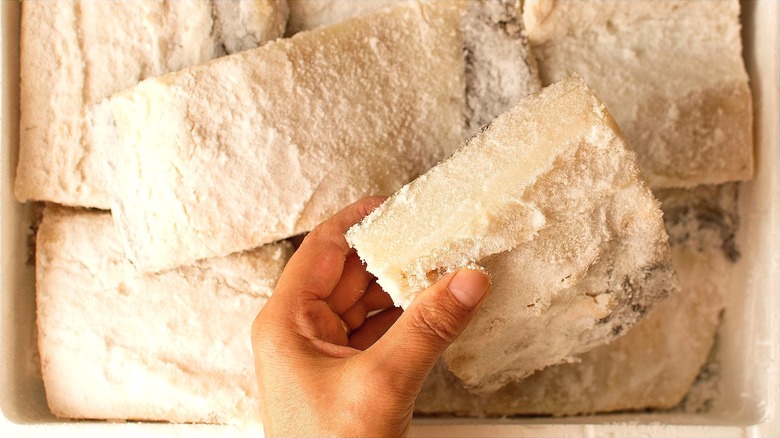 Hand holding a salted codfish fillet over many more fillets