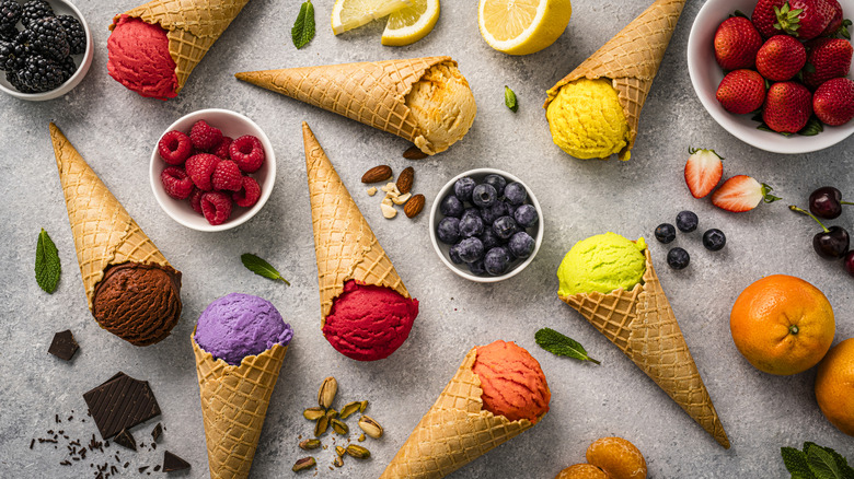 Various flavors of ice cream surrounded by berries and other toppings on a gray background