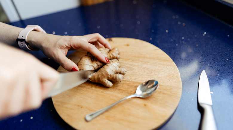 A person's hands are seen cutting ginger with a knife.