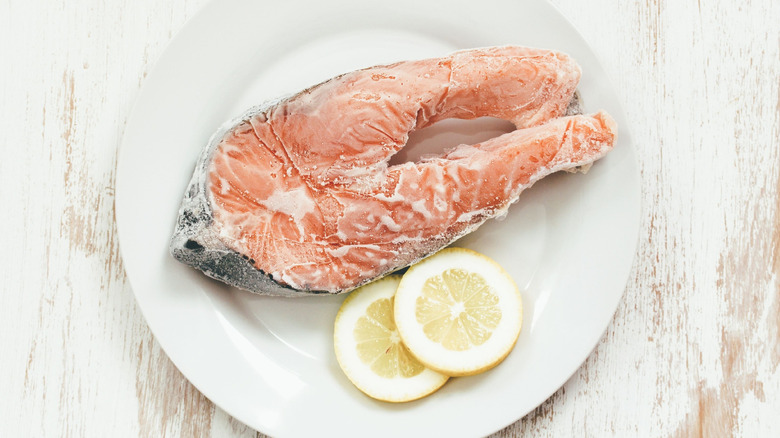 frozen salmon in packaging on a white plate with lemon slices