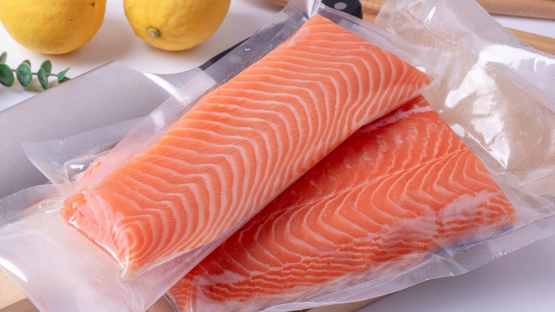 Salmon slices in sealed vacuum bag with two lemons and a knife in the background