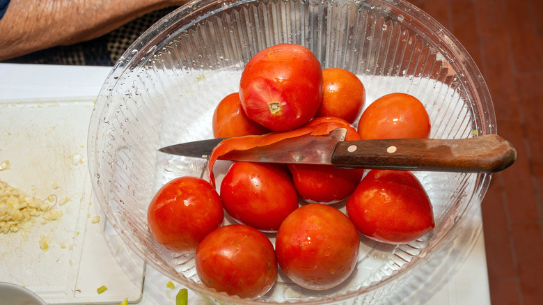 A batch of tomatoes in a glass bowl with a knife on top