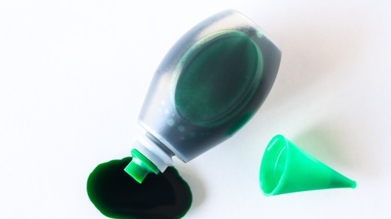 St. Patricks green beer in stein on wood table surrounded by beads and lucky charm.