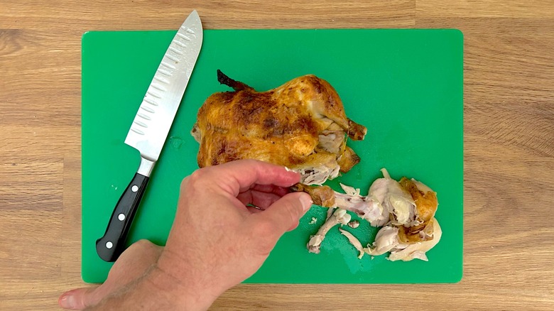 Removing the leg bone from a rotisserie chicken by hand that is resting on a cutting board