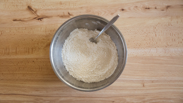 A mixing bowl with a fork sitting in a mixture of flour and salt on a wooden table.