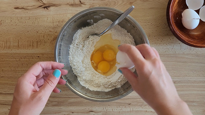 Hands cracking eggs into a bowl of flour