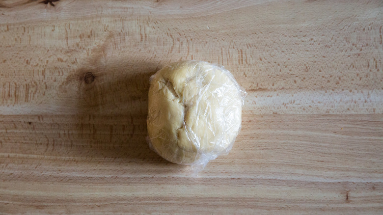 A plastic-wrapped ball of pasta dough sitting on a tabletop.