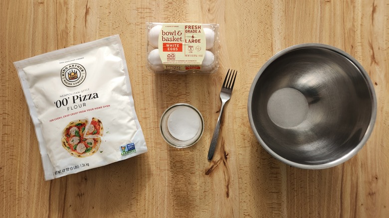 Ingredients and tools for making fresh pasta dough are arranged on a wooden table.