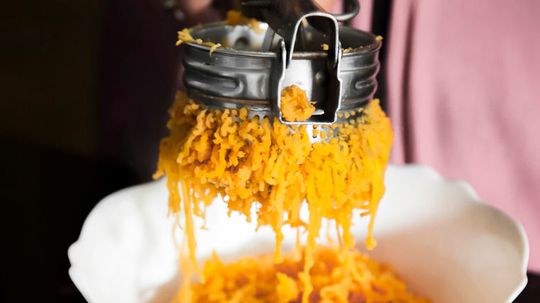 Root vegetables being pushed through a ricer