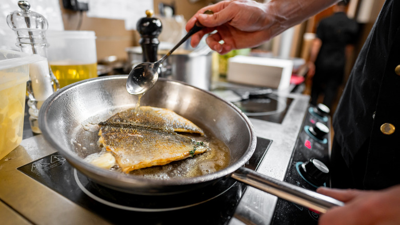 Chef cooking fish in a stainless steel pan