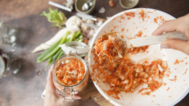Kimchi preparation, with mixed ingredients being transferred from a bowl to a jar