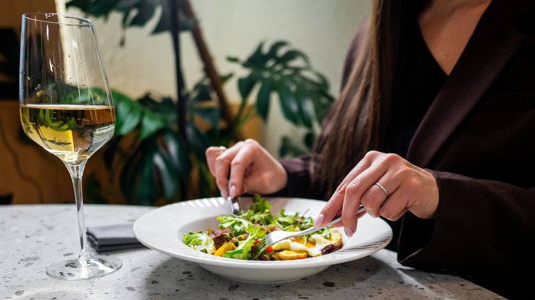 A person enjoys a fresh salad and a glass of white wine in an elegant dining setting
