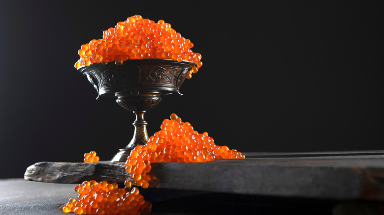 Salmon fish roe in a small bowl on a wooden board with more salmon roe