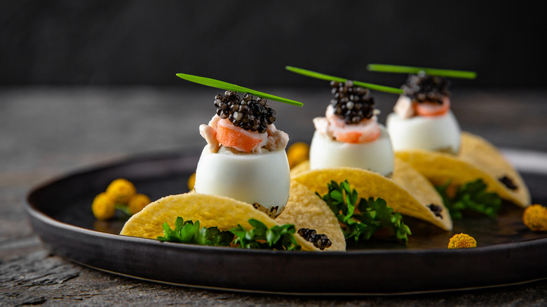 A plate of appetizers featuring potato chips, hard boiled eggs, shrimp, and caviar