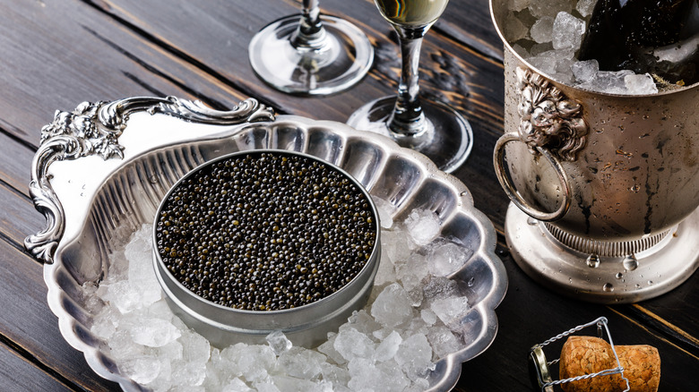 A tin of black caviar on ice with champagne