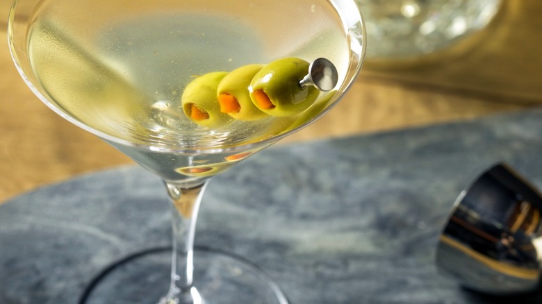 A dirty martini served up in a martini glass and garnished with three olives on a skewer.