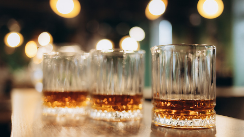A variety of bourbons in tumbler glasses on a bartop.