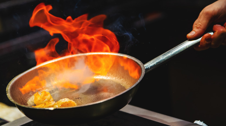 A chef flambéing a pan of shrimps.