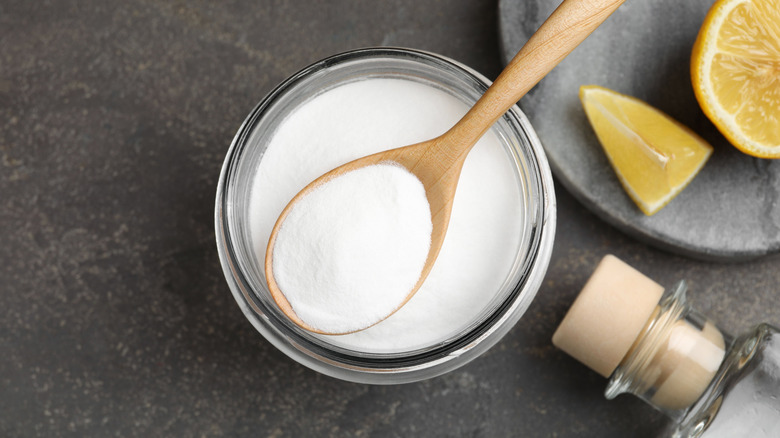 A glass jar filled with baking soda next to a bottle of white vinegar.