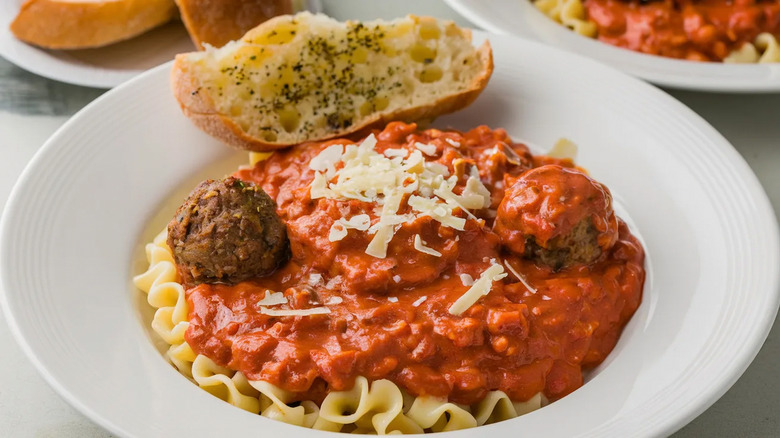 Tomato sauce and meatballs over pasta with garlic bread on a white plate