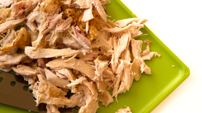 Shredded rotisserie chicken on a green cutting board