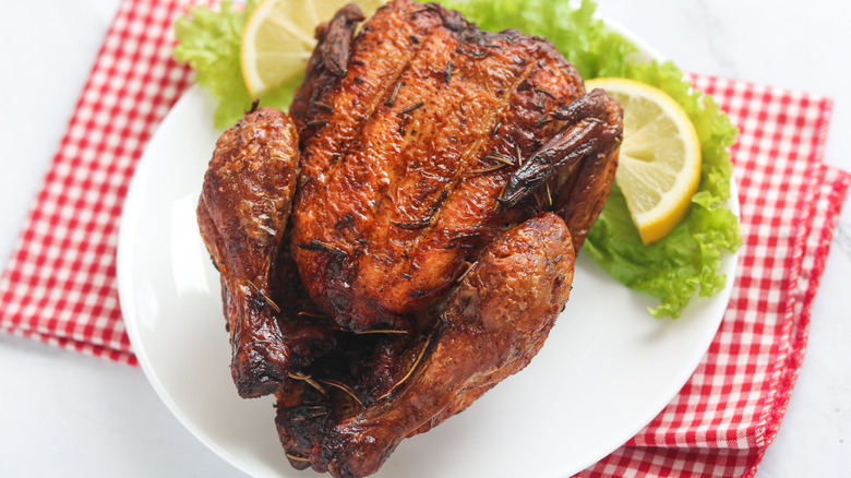 Rotisserie chicken on a white plate with lettuce and lemon for garnish
