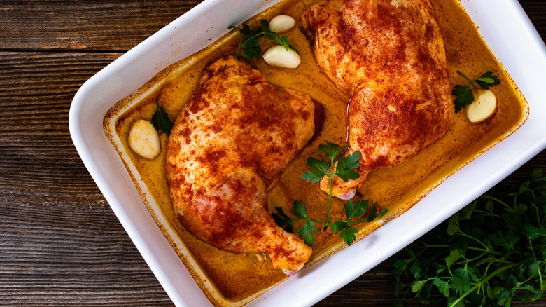 A baking dish with two chicken thighs marinating with garlic and parsley.