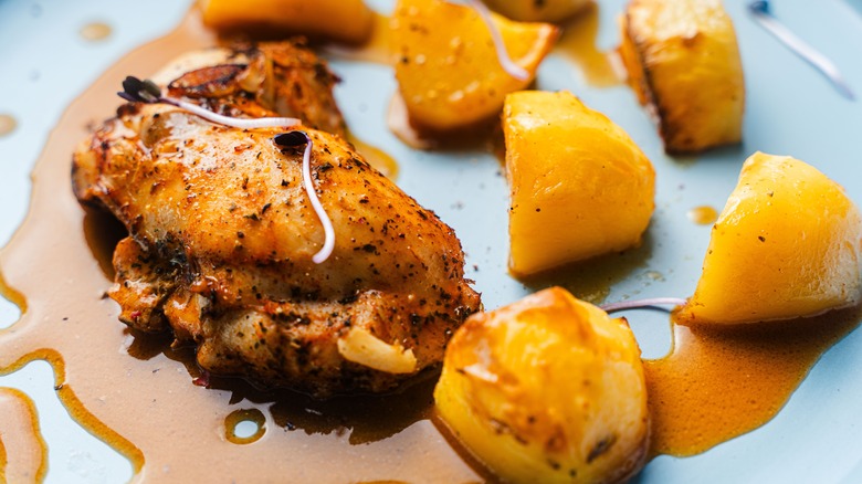 A baked chicken thigh and potatoes covered in a thick, sticky sauce.