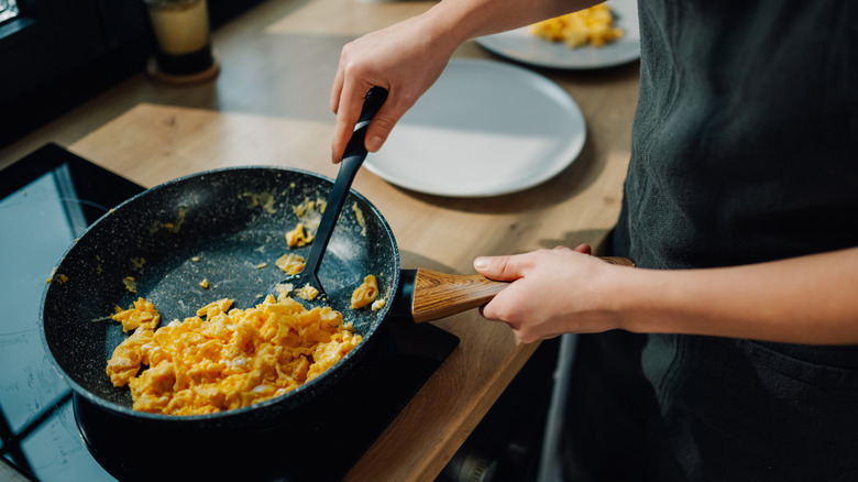 A chef stirring scrambled eggs on a stove.
