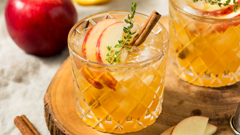 A bourbon cocktail is garnished with thinly sliced apples, all in a pretty rocks glass.