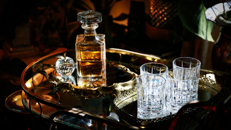 A pretty decanter of bourbon is arranged on a bar cart with a crystal apple and glasses in a distinguished scene.