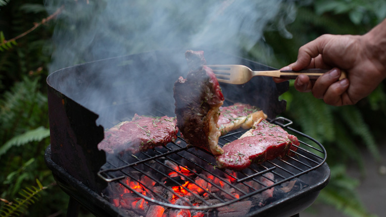 Flipping meat on a charcoal grill.