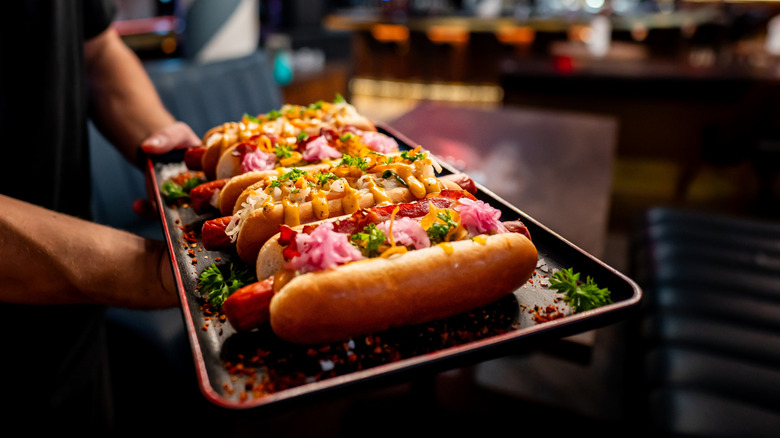 A closeup of four garnished hot dogs on a tray
