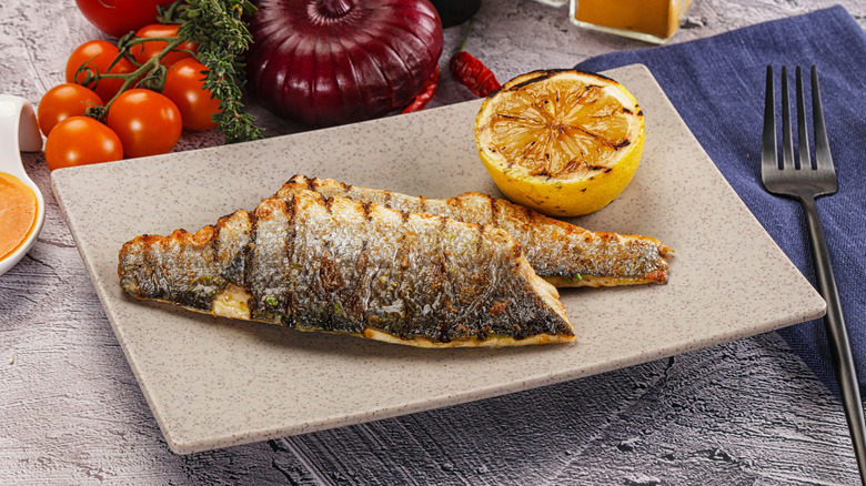 Grilled sea bass fillet with crispy skin on a plate with a grilled lemon