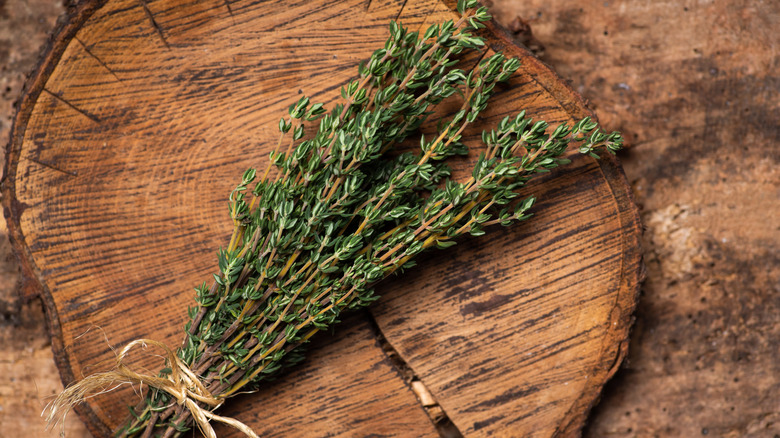 A bunch of thyme is tied with twine and sits on a wooden cutting board.