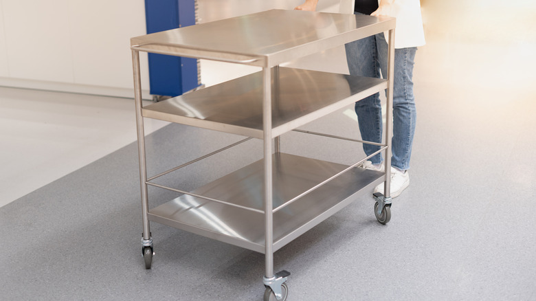 A person is pushing a metal prep table.